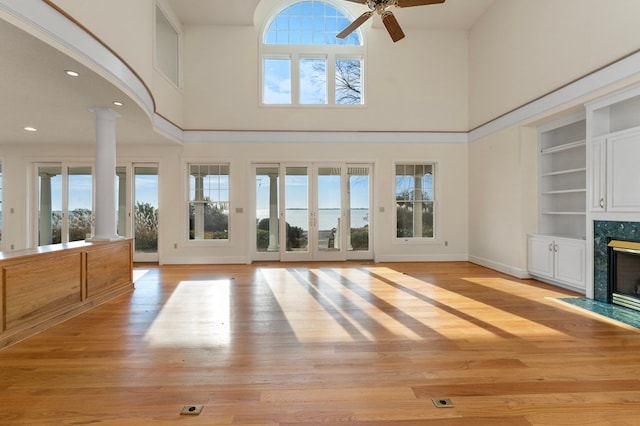 unfurnished living room with ceiling fan, a high ceiling, a premium fireplace, built in features, and decorative columns