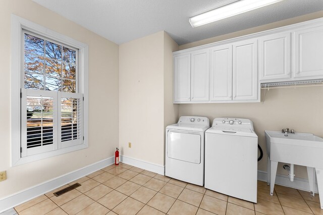 clothes washing area with cabinets, a textured ceiling, sink, independent washer and dryer, and light tile patterned flooring