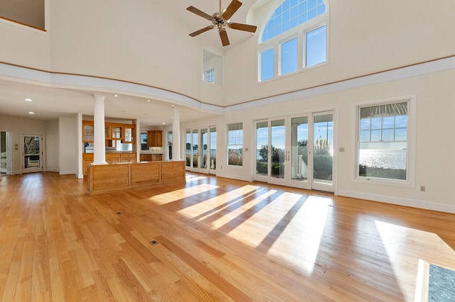 unfurnished living room with ornate columns, ceiling fan, light hardwood / wood-style flooring, and a high ceiling