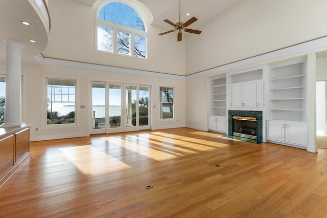 unfurnished living room featuring built in shelves, ceiling fan, a towering ceiling, and a high end fireplace