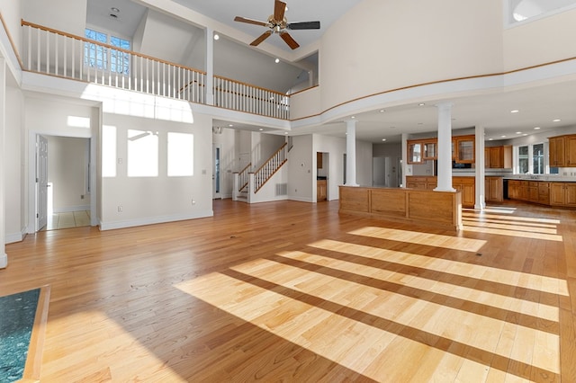 unfurnished living room featuring decorative columns, ceiling fan, a high ceiling, and light wood-type flooring