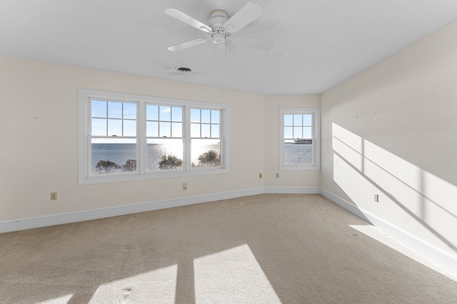 carpeted spare room featuring ceiling fan, a water view, and a textured ceiling