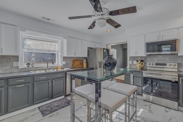 kitchen featuring appliances with stainless steel finishes, gray cabinetry, backsplash, white cabinets, and sink