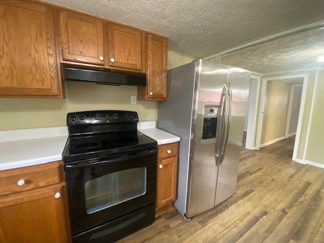 3097 Oakland Rd, Farnham, VA 22460 - kitchen with black range with electric stovetop, under cabinet range hood, stainless steel fridge, brown cabinetry, and light countertops