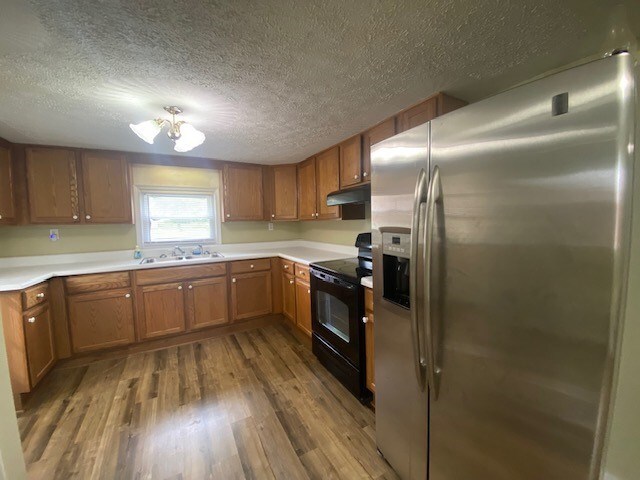 3097 Oakland Rd, Farnham, VA 22460 - kitchen with stainless steel refrigerator with ice dispenser, black range with electric stovetop, under cabinet range hood, wood finished floors, and a textured ceiling