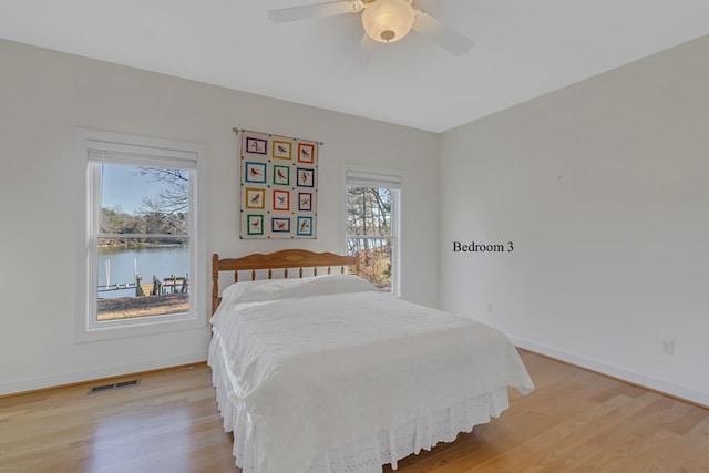 bedroom featuring ceiling fan, a water view, and light wood-type flooring