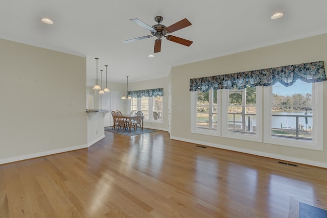 unfurnished living room with ceiling fan with notable chandelier, a water view, and light wood-type flooring