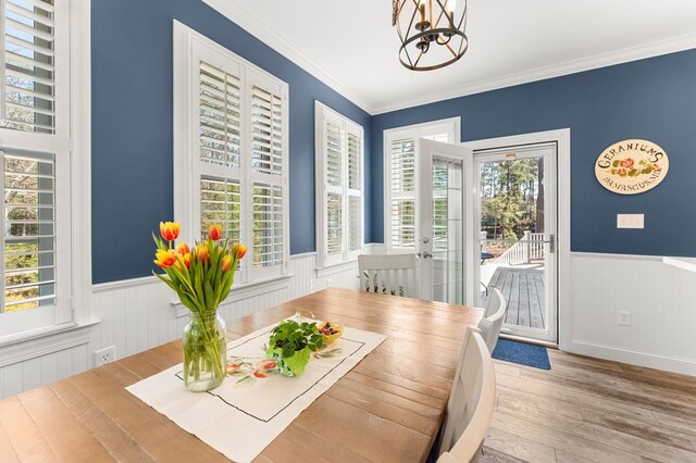 dining room featuring a healthy amount of sunlight, wood finished floors, wainscoting, and ornamental molding