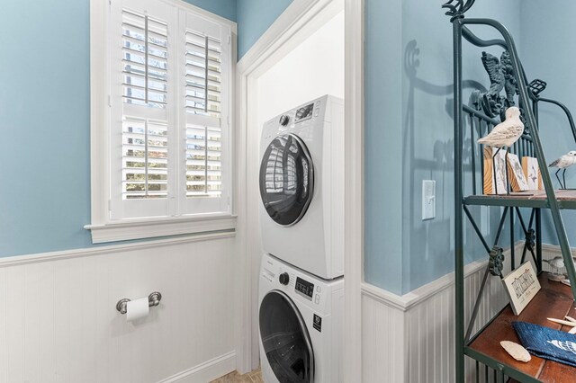 washroom with laundry area, stacked washer and dryer, and wainscoting