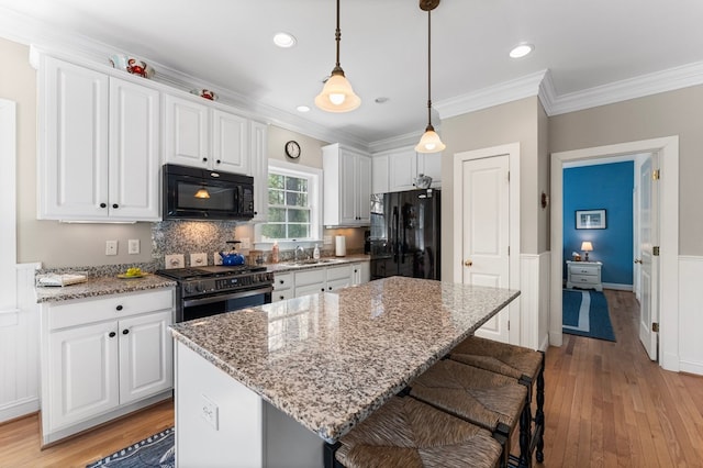 kitchen with a sink, black appliances, white cabinets, and light wood finished floors