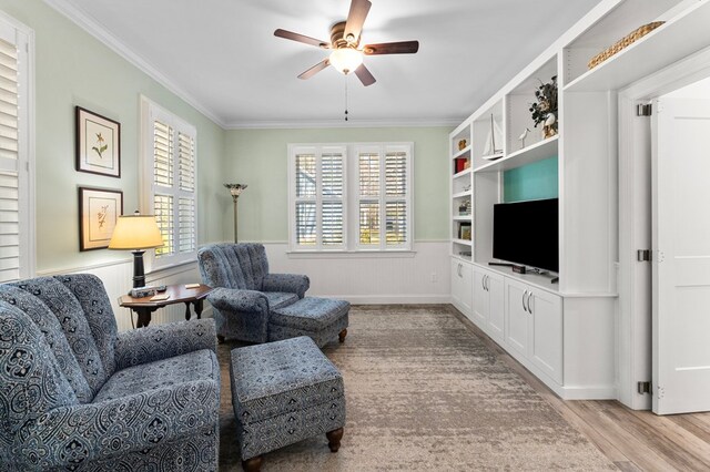 living room with ceiling fan, light wood-type flooring, a wainscoted wall, and ornamental molding