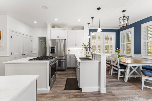 kitchen featuring a wainscoted wall, light wood finished floors, a sink, appliances with stainless steel finishes, and crown molding