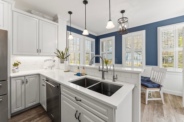 kitchen featuring ornamental molding, a sink, wood finished floors, stainless steel appliances, and a peninsula