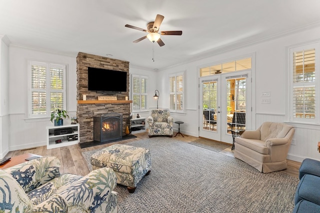 living room featuring a stone fireplace, french doors, light wood-type flooring, and ornamental molding