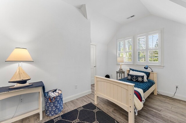 bedroom with visible vents, lofted ceiling, baseboards, and wood finished floors