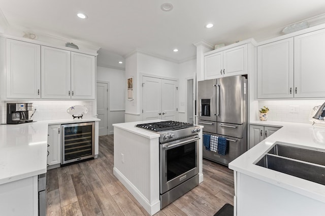 kitchen with beverage cooler, a sink, premium appliances, wood finished floors, and white cabinets