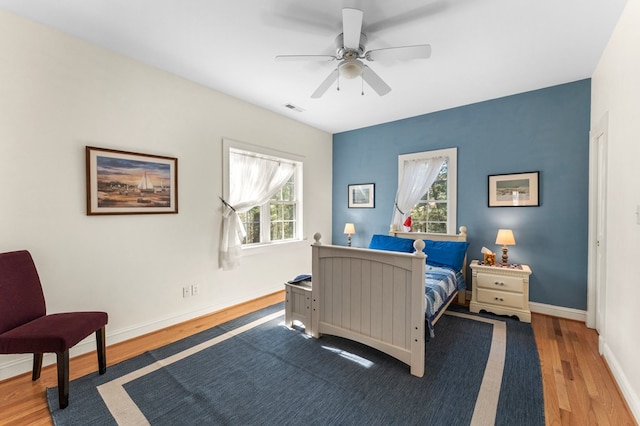 bedroom with a ceiling fan, wood finished floors, visible vents, and baseboards