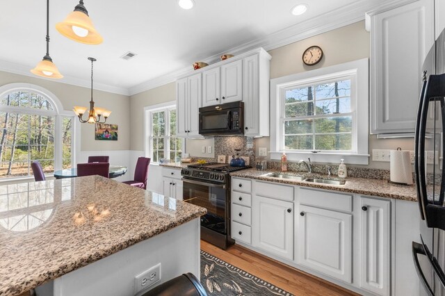 kitchen featuring light wood-style flooring, a sink, black appliances, white cabinetry, and crown molding