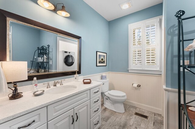 bathroom with wood finished floors, visible vents, a wainscoted wall, stacked washing maching and dryer, and toilet