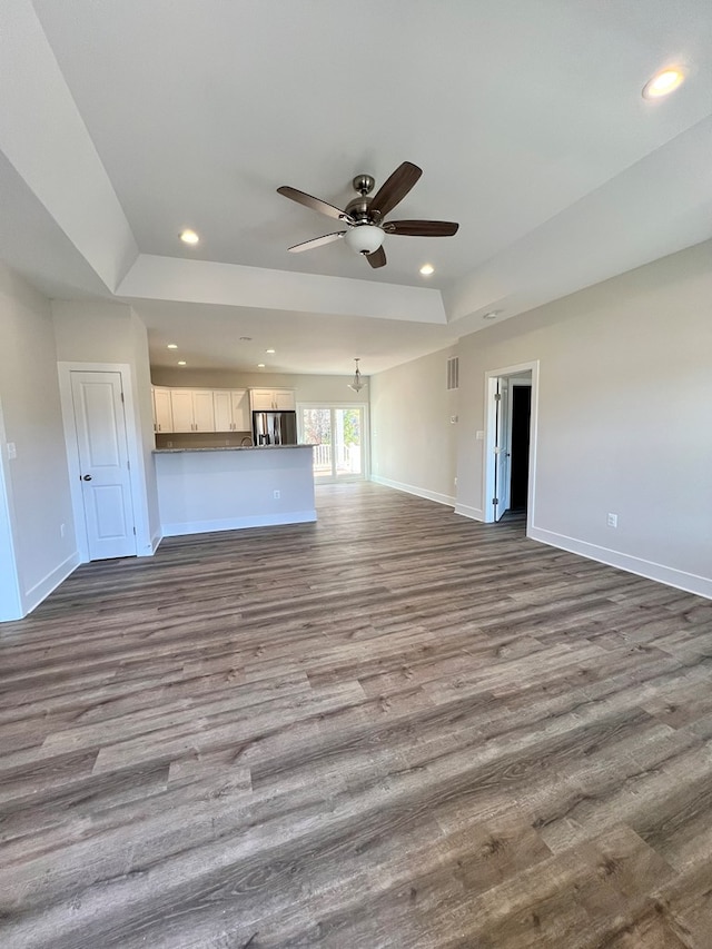 unfurnished living room with wood-type flooring, a raised ceiling, and ceiling fan