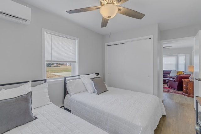 bedroom with ceiling fan, light hardwood / wood-style floors, a wall unit AC, and a closet