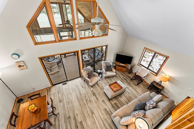 living room with ceiling fan, a towering ceiling, and light wood-type flooring