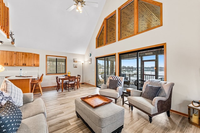 living room with high vaulted ceiling, light hardwood / wood-style floors, ceiling fan, and a water view