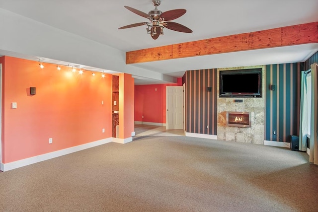 unfurnished living room featuring beam ceiling, ceiling fan, track lighting, a fireplace, and carpet