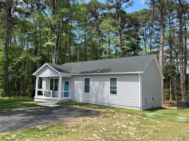 view of front of house with covered porch, a front lawn, and roof with shingles