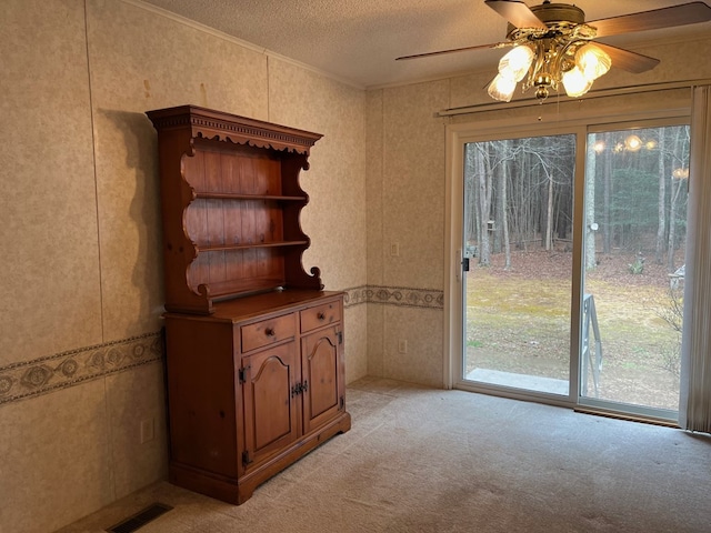 unfurnished dining area featuring ceiling fan, ornamental molding, light colored carpet, and a textured ceiling