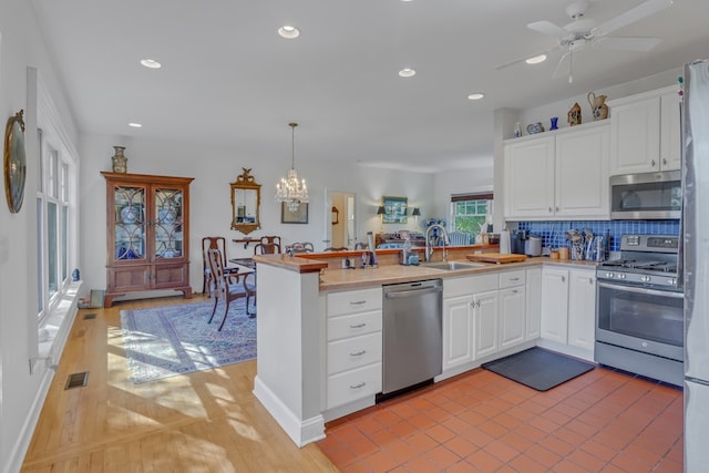 kitchen featuring kitchen peninsula, appliances with stainless steel finishes, white cabinets, and hanging light fixtures