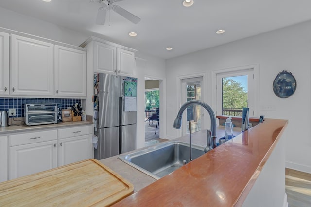 kitchen featuring tasteful backsplash, ceiling fan, sink, white cabinets, and stainless steel refrigerator