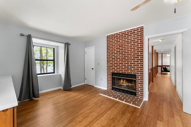 unfurnished living room with a fireplace, a ceiling fan, light wood-style flooring, and baseboards