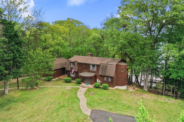 view of front facade featuring a front yard, a gambrel roof, an outdoor structure, a chimney, and roof with shingles