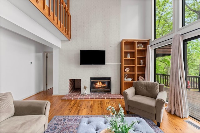 living room featuring a brick fireplace, a towering ceiling, visible vents, and wood finished floors