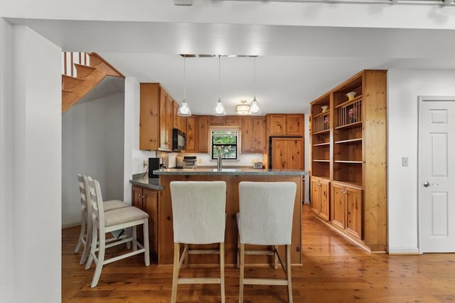 kitchen featuring brown cabinets, light wood-style floors, black microwave, decorative light fixtures, and a peninsula