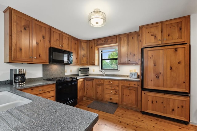 kitchen featuring brown cabinets, light wood-type flooring, black appliances, a toaster, and dark countertops