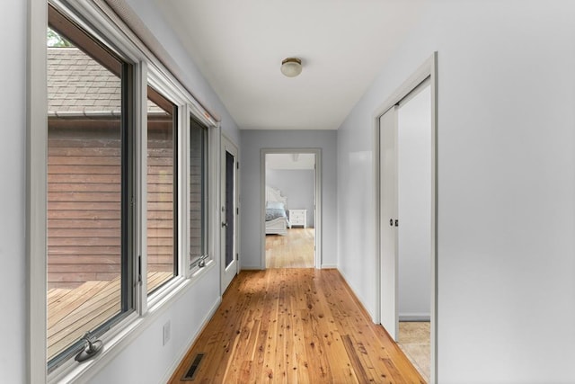 corridor with baseboards, light wood-type flooring, and plenty of natural light