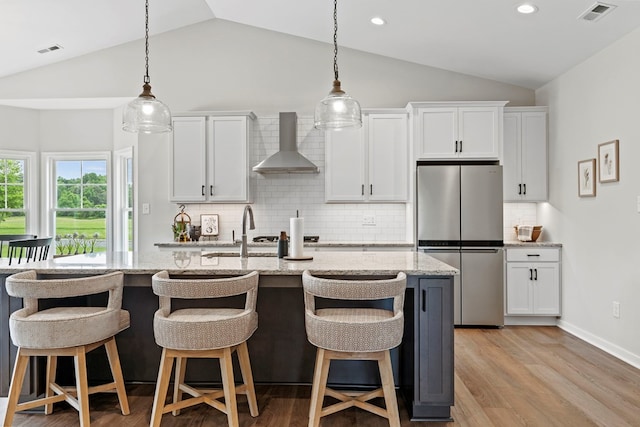 kitchen with white cabinets, wall chimney exhaust hood, stainless steel fridge, and tasteful backsplash