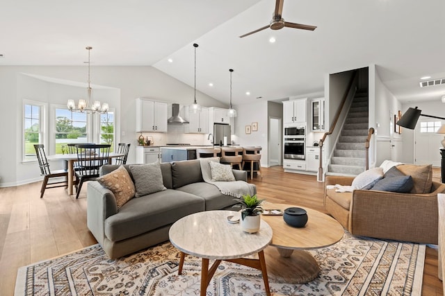 living room with ceiling fan with notable chandelier, light hardwood / wood-style floors, and high vaulted ceiling