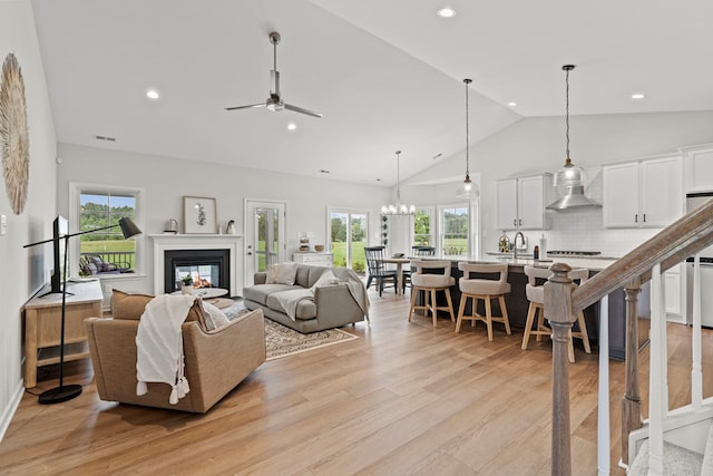 living room with sink, high vaulted ceiling, ceiling fan with notable chandelier, and light wood-type flooring