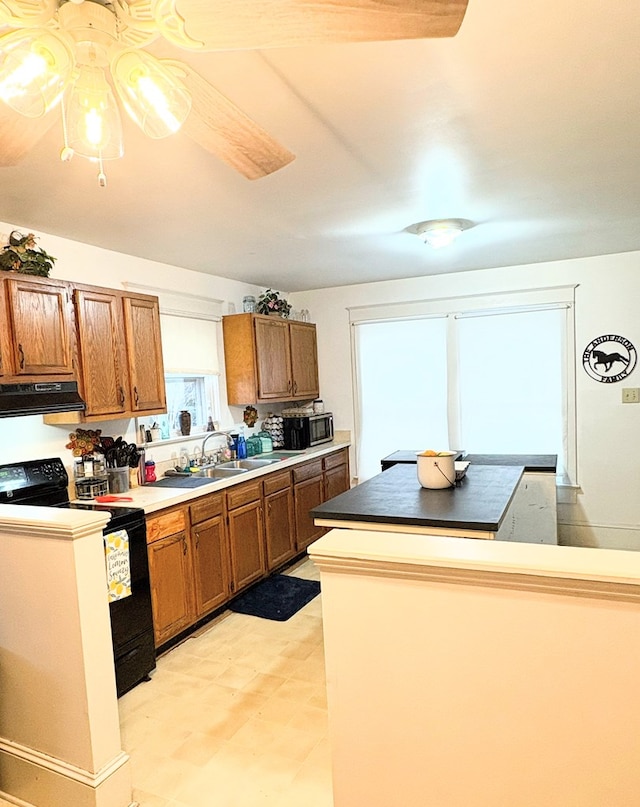 kitchen featuring stainless steel microwave, brown cabinets, black electric range oven, a sink, and exhaust hood