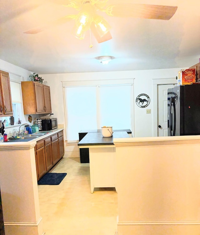 kitchen featuring brown cabinetry, stainless steel microwave, black fridge with ice dispenser, and a sink