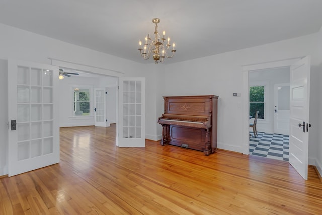 misc room featuring french doors, ceiling fan with notable chandelier, and light hardwood / wood-style flooring