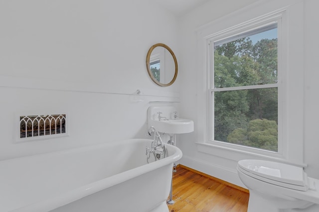 bathroom featuring a wealth of natural light, a washtub, wood-type flooring, and toilet