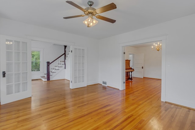 spare room with french doors, ceiling fan with notable chandelier, and light hardwood / wood-style floors