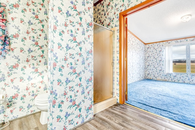 bathroom featuring crown molding, wood-type flooring, a shower with shower door, and toilet