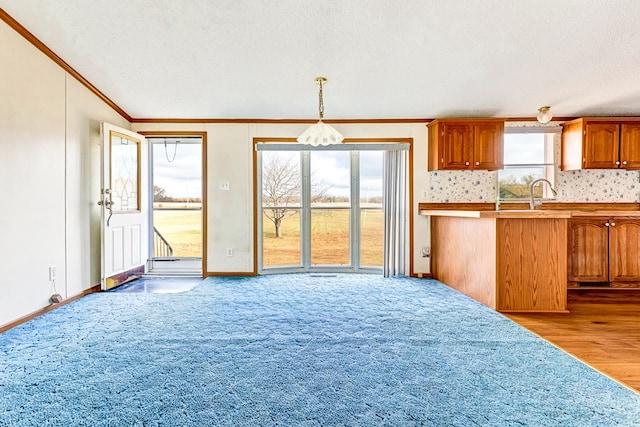 kitchen featuring a textured ceiling, crown molding, light wood-type flooring, and hanging light fixtures