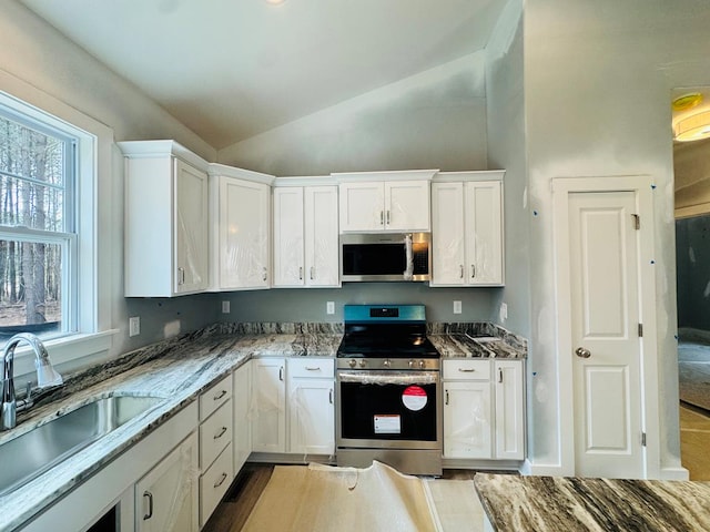 kitchen featuring a sink, light stone counters, white cabinetry, appliances with stainless steel finishes, and lofted ceiling