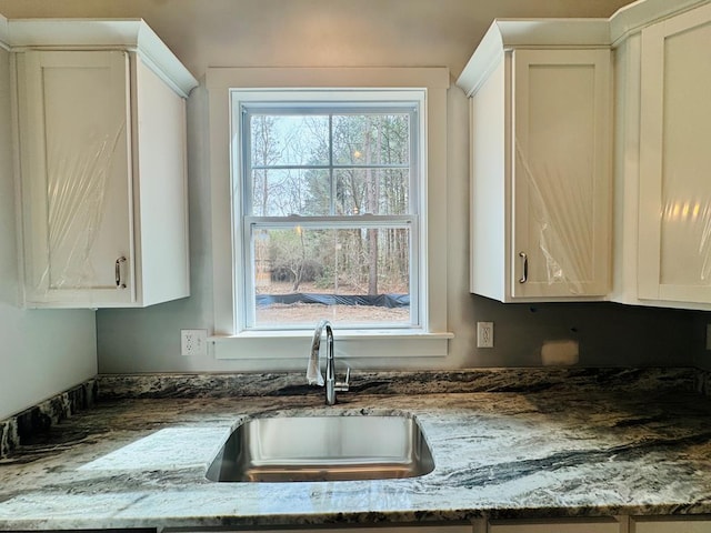 kitchen with stone countertops, white cabinetry, and a sink